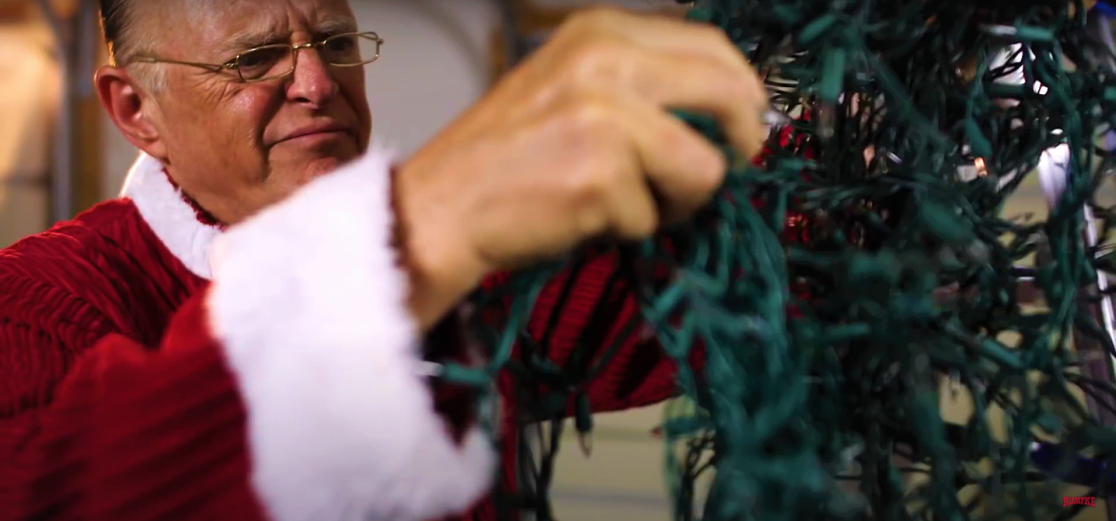 Man In Santa Costume Holding Old Christmas Lights Near Recycling Bin